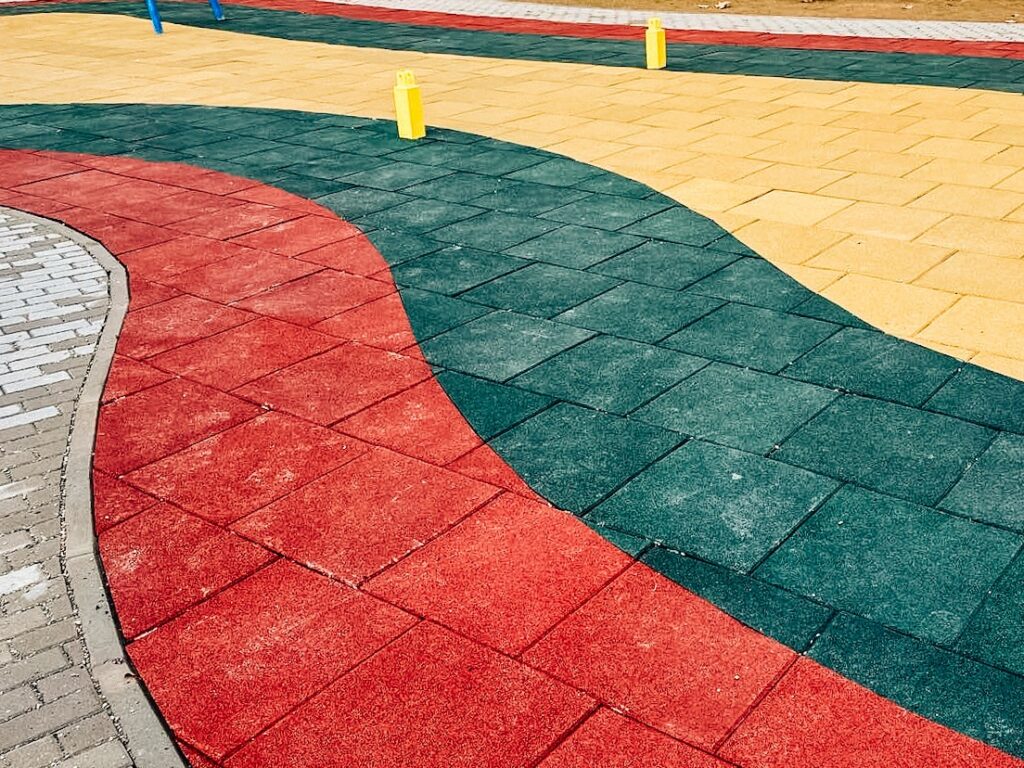 Interlocking Hum-Tech rubber safety tiles used on a commercial playground using red green and yellow to create a vibrant pattern